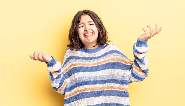 Giovane bella ragazza che scrolla le spalle con un'espressione stupida, pazza, confusa e perplessa, sentendosi infastidita e all'oscuro