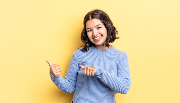 Young pretty girl smiling cheerfully and casually pointing to copy space on the side feeling happy and satisfied