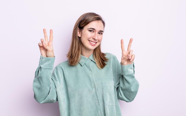 笑顔で幸せそうに見える、フレンドリーで満足している若いかわいい女の子、両手で勝利または平和を身振りで示す