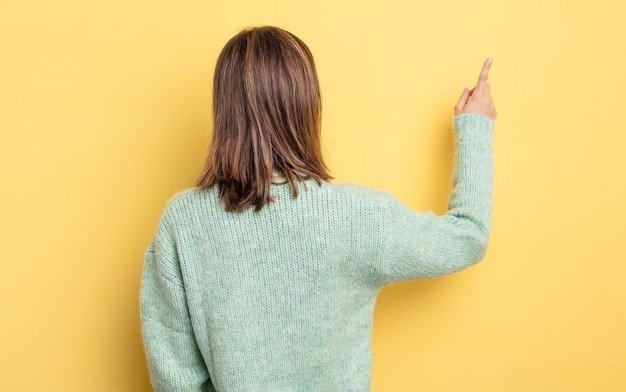 Giovane bella ragazza in piedi e che punta a un oggetto sulla vista posteriore dello spazio di copia