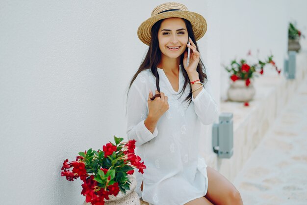 young and pretty girl in a summer city sitting near flowers with smartphone