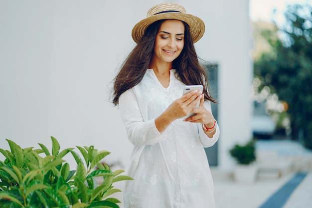 若い、美しい女の子、スマートフォンで夏の街に立っている