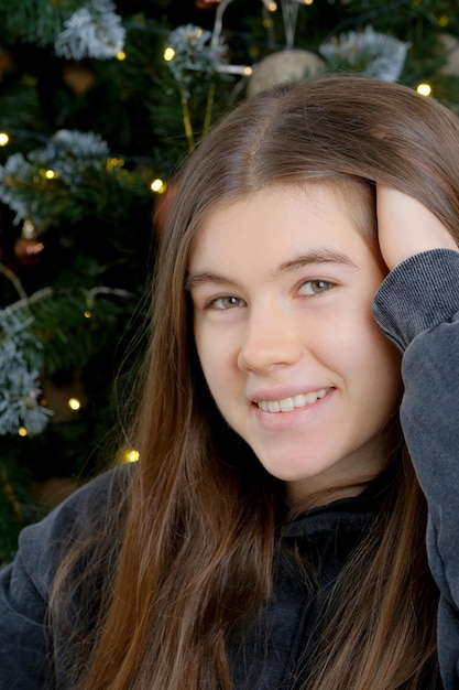 Photo young pretty girl with long hair in a dark hoodie portrait next to a decorated christmas tree