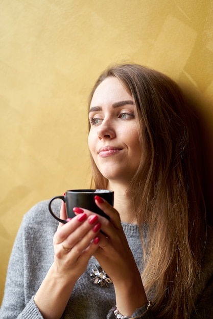 Young pretty girl with long hair drinking coffee or tea  in the cafe.