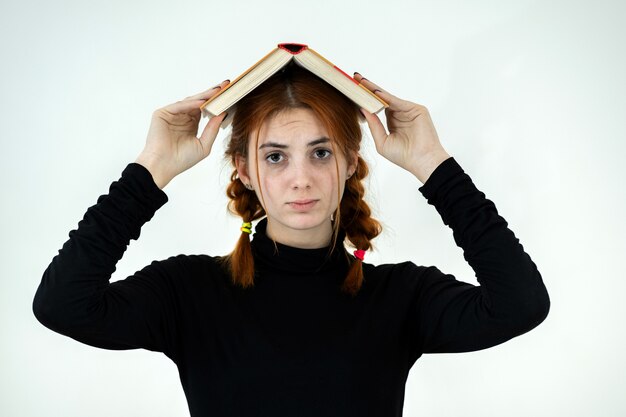 Молодая милая девушка с открытой книгой на ее голове. Концепция чтения и образования.