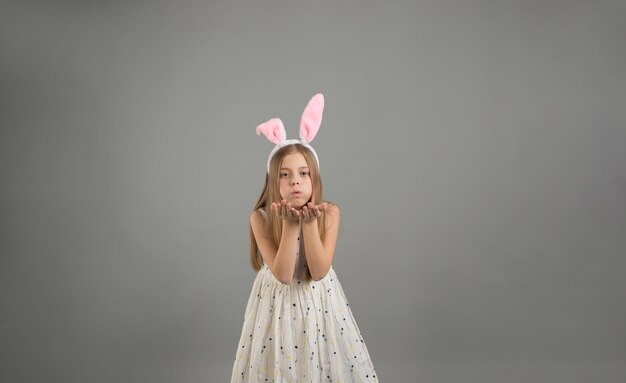 A young pretty girl with rabbit ears poses merrily on a gray background air kiss