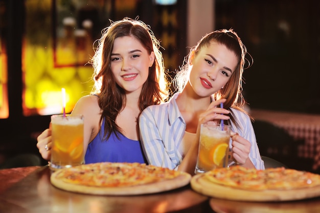 若い可愛い女の子がピザを食べて、バーやピッツェリアでビールやビールカクテルを飲む