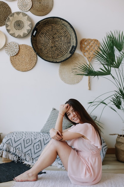 Young pretty happy woman in a dress sitting down in exotic boho interior