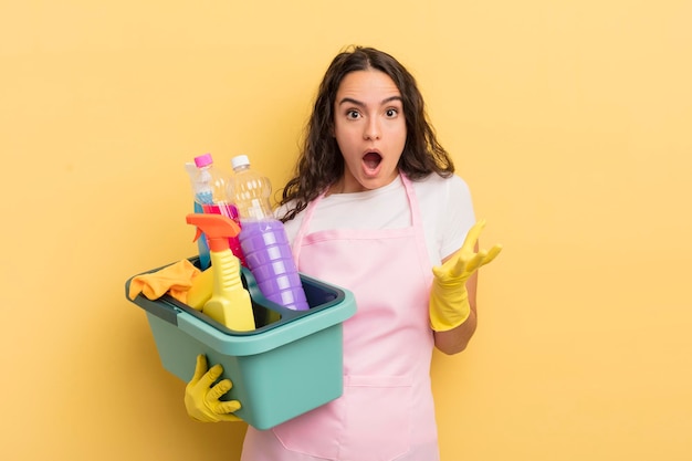 Young pretty hispanic woman amazed shocked and astonished with an unbelievable surprise housework an clean products concept