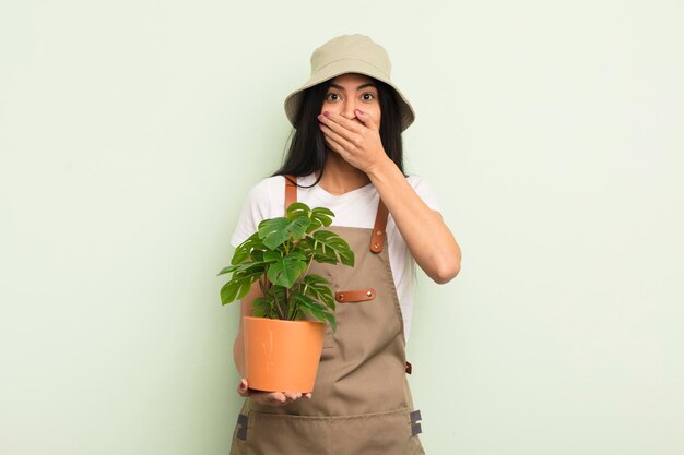 Молодая симпатичная латиноамериканка, закрывающая рот руками, шокирована концепцией фермера или садовника