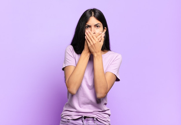 Young pretty hispanic woman covering mouth with hands with a shocked, surprised expression, keeping a secret or saying oops