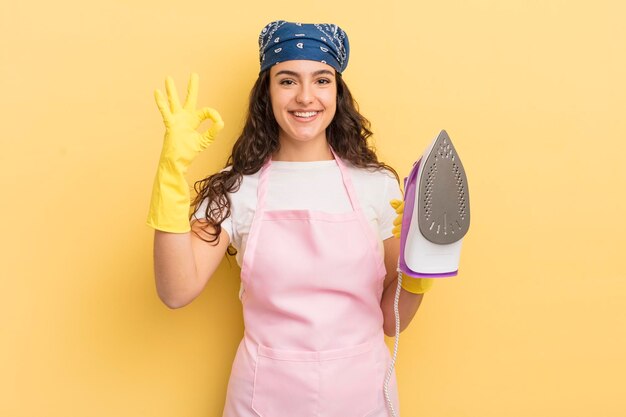 Young pretty hispanic woman feeling happy showing approval with okay gesture iron and clothes concept