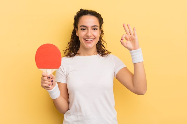 Young pretty hispanic woman feeling happy, showing approval with okay gesture. ping pong concept