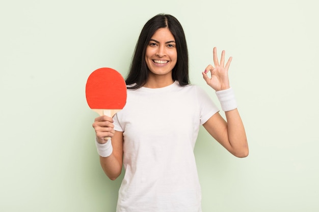 Young pretty hispanic woman feeling happy showing approval with okay gesture ping pong concept