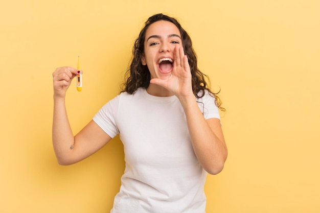 Young pretty hispanic woman feeling happygiving a big shout out with hands next to mouth thermometer concept