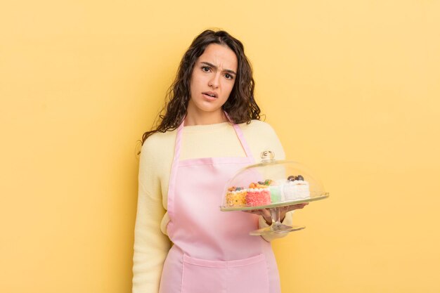 Young pretty hispanic woman feeling puzzled and confused chef and cakes concept