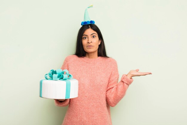 Young pretty hispanic woman feeling puzzled and confused and doubting birthday cake concept