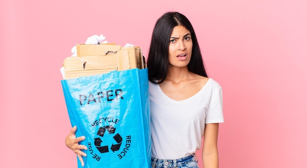 困惑して混乱していると感じ、リサイクルするために紙袋を持っている若いかなりヒスパニック系の女性