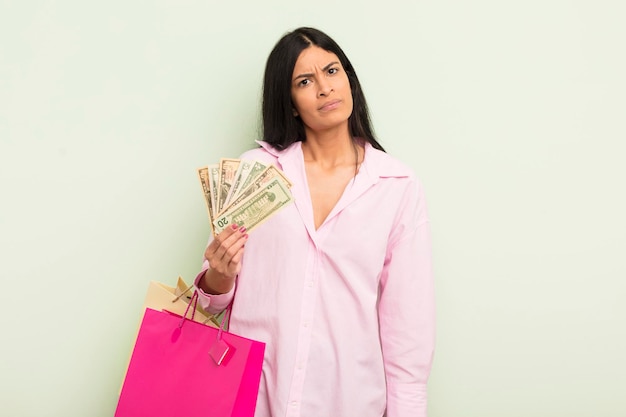 Young pretty hispanic woman feeling puzzled and confused. shopping bags concept