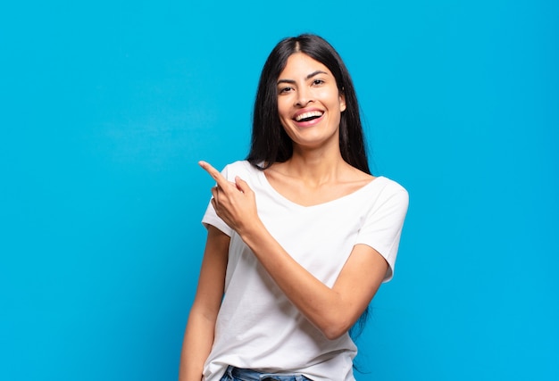 Young pretty hispanic woman looking excited and surprised pointing to the side and upwards to copy space