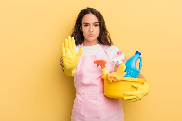 Young pretty hispanic woman looking serious showing open palm making stop gesture housework an clean products concept