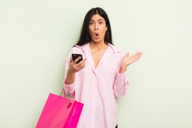 Young pretty hispanic woman looking surprised and shocked with jaw dropped holding an object shopping bags concept