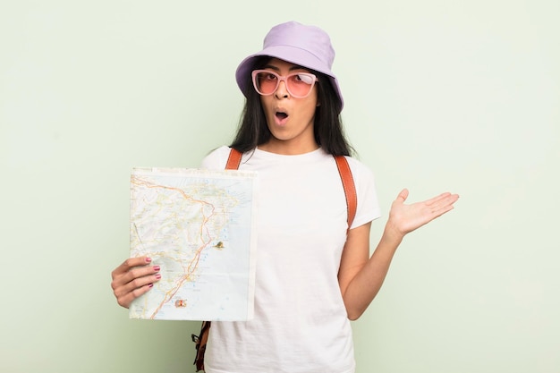 Young pretty hispanic woman looking surprised and shocked with jaw dropped holding an object tourist and map concept