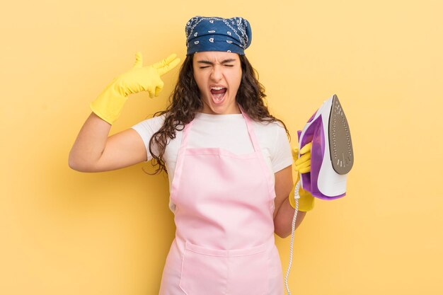 Young pretty hispanic woman looking unhappy and stressed suicide gesture making gun sign iron and clothes concept