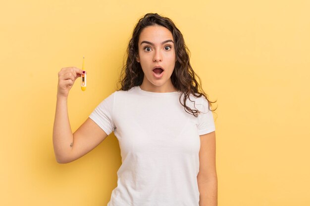 Young pretty hispanic woman looking very shocked or surprised. thermometer concept