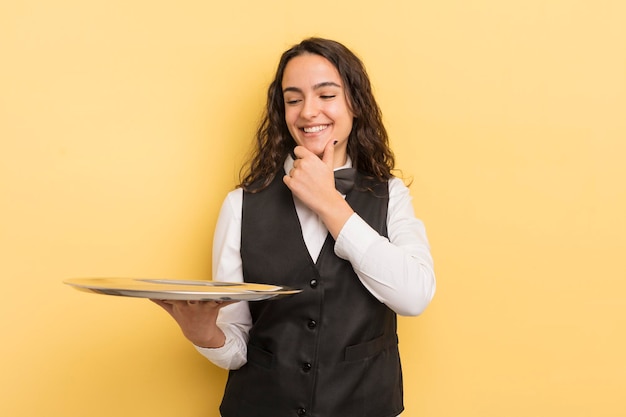 Young pretty hispanic woman pointing at camera choosing you waiter and tray concept
