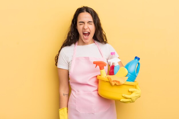 Young pretty hispanic woman shouting aggressively looking very angry housework an clean products concept