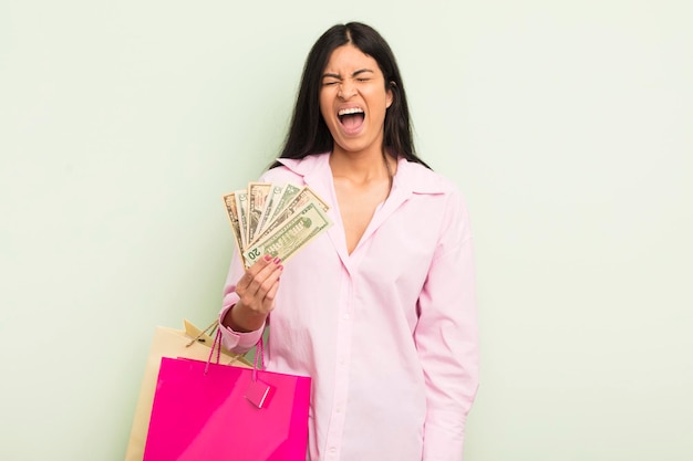 Young pretty hispanic woman shouting aggressively looking very angry shopping bags concept