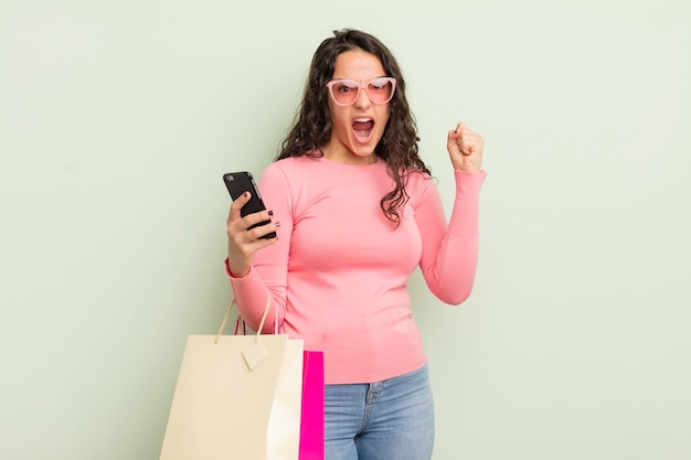 Young pretty hispanic woman shouting aggressively with an angry expression shopping bags concept