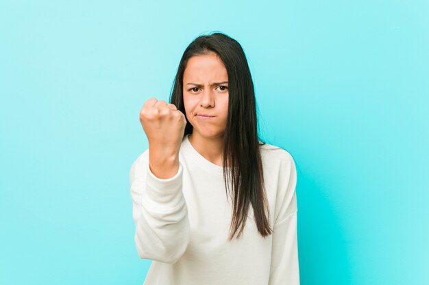Young pretty hispanic woman showing fist to camera, aggressive facial expression.