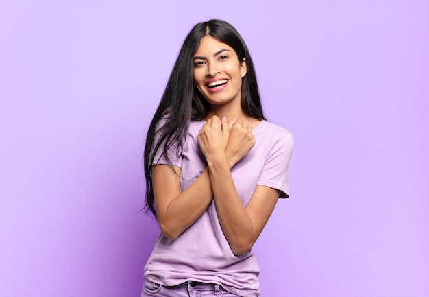 Young pretty hispanic woman smiling cheerfully and celebrating, with fists clenched and arms crossed, feeling happy and positive