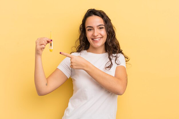 Young pretty hispanic woman smiling cheerfully feeling happy and pointing to the side thermometer concept