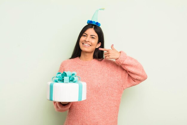 Young pretty hispanic woman smiling confidently pointing to own broad smile birthday cake concept