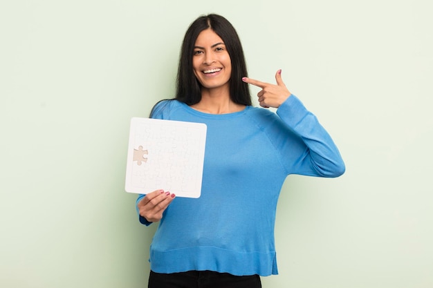 Young pretty hispanic woman smiling confidently pointing to own broad smile puzzle concept