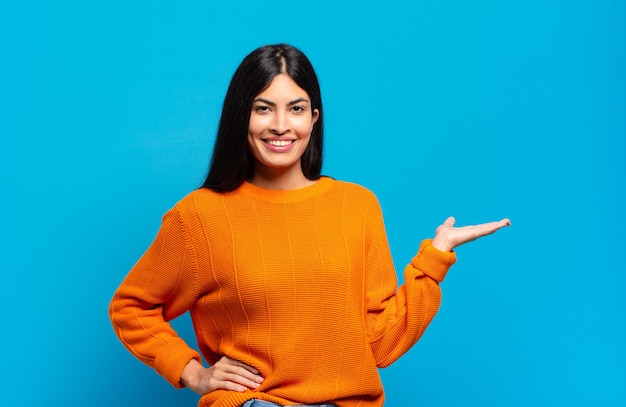 Young pretty hispanic woman smiling, feeling confident, successful and happy, showing concept or idea on copy space on the side