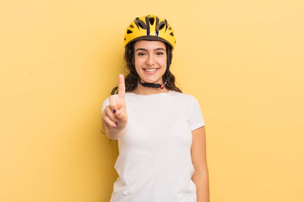 Young pretty hispanic woman smiling and looking friendly, showing number one. bycicle concept