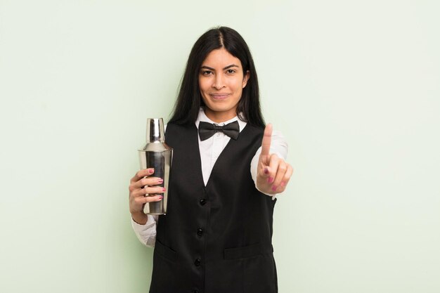 Young pretty hispanic woman smiling and looking friendly showing number one cocktail bartender concept