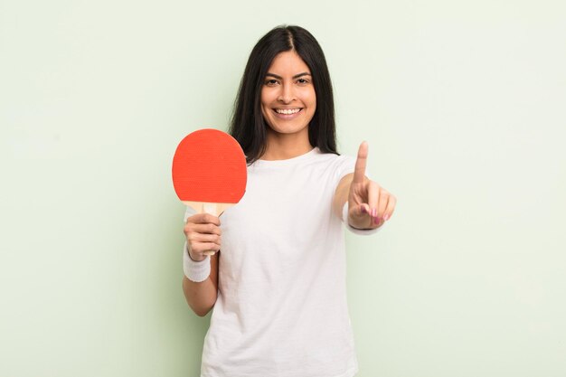 Young pretty hispanic woman smiling and looking friendly showing number one ping pong concept