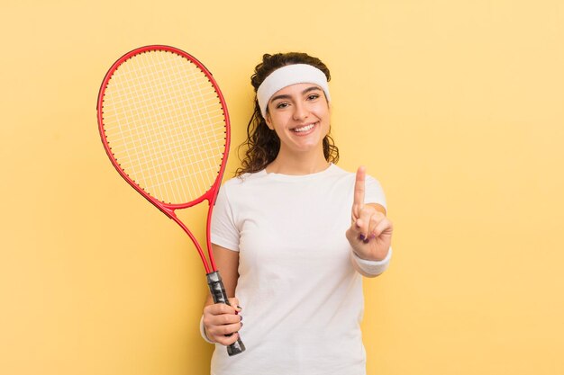 Young pretty hispanic woman smiling and looking friendly showing number one tennis concept