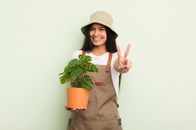Молодая симпатичная латиноамериканка улыбается и выглядит дружелюбно, показывая концепцию фермера или садовника номер два