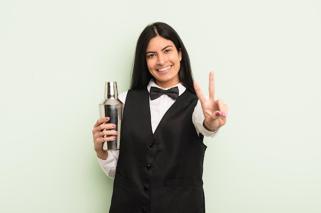 Young pretty hispanic woman smiling and looking happy gesturing victory or peace cocktail bartender concept