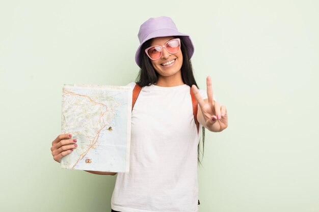 Young pretty hispanic woman smiling and looking happy gesturing victory or peace tourist and map concept