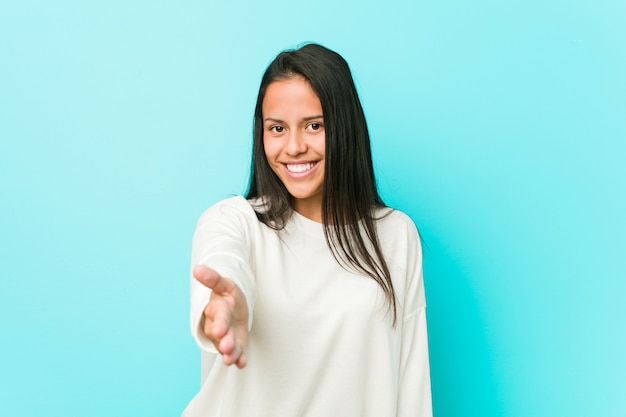 Young pretty hispanic woman stretching hand at camera in greeting gesture.