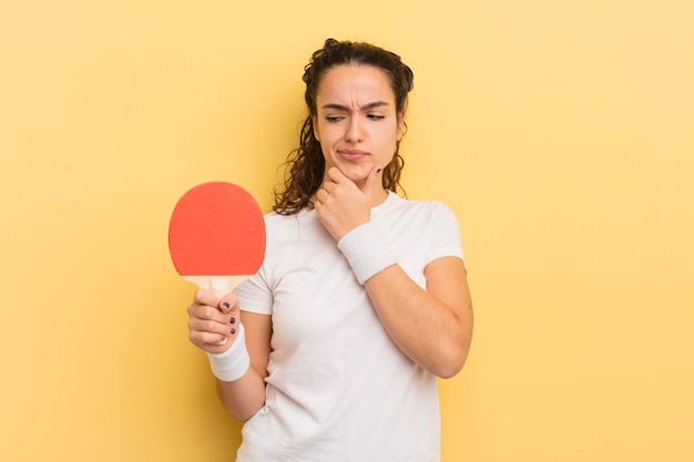 young pretty hispanic woman thinking, feeling doubtful and confused. ping pong concept