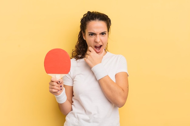 Young pretty hispanic woman with mouth and eyes wide open and hand on chin. ping pong concept