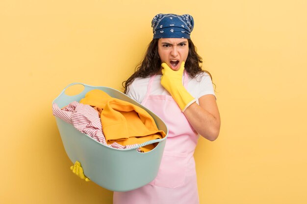 Young pretty hispanic woman with mouth and eyes wide open and hand on chin wash and clothes concept